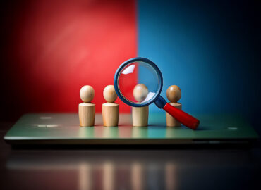 A magnifying glass focuses on one wooden figure in a row of five on a laptop, symbolizing the importance of finding the right candidate. A magnifying glass focuses on one wooden figure in a row of five on a laptop, symbolizing the importance of finding the right candidate.